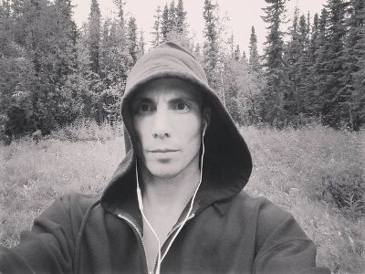 Tucker Dee Chapman is wearing hoodie, airphones and is in the woods.
